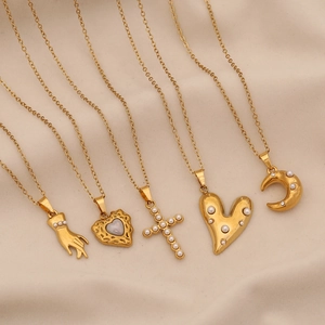 Detail of five gold necklaces featuring pearl, heart, cross and moon charms on beige fabric