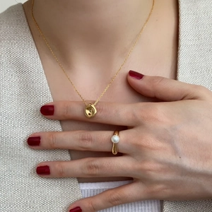 Detail of irregular gold lava texture pendant necklace and pearl ring on female model