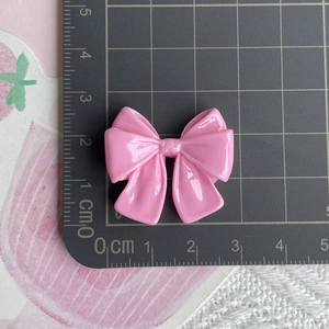 Top-view of a pink resin bow accessory on a scale mat showing size measurements