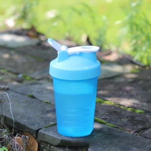 Outdoor close-up of blue translucent protein shaker bottle with flip-top lid and handle