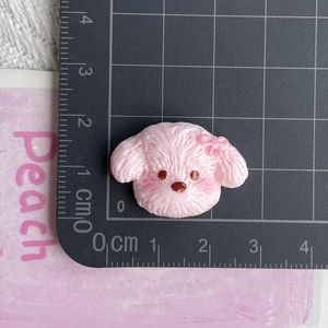 Detail view of a pink resin dog charm showing size dimensions with a ruler
