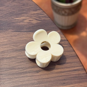 Gros plan d'une pince à cheveux fleur crème avec ressort doré sur bois foncé