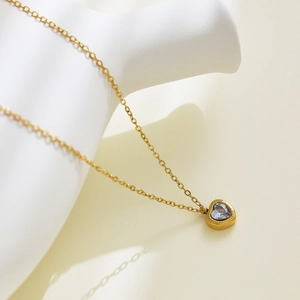 Close-up of 18k gold heart necklace featuring a lavender zircon stone on a white display