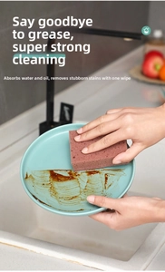 Close-up of pink honeycomb sponge cleaning grease stains on a ceramic plate in a kitchen