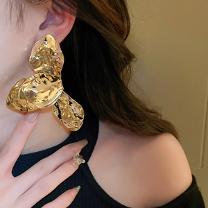 Close-up of a large textured gold floral earring worn by a model in a stylish setting