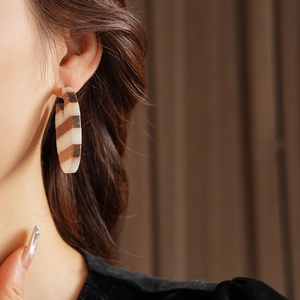 Close-up of model wearing large striped resin hoop earrings in white and brown wood tones