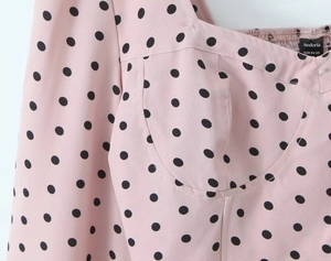 Détail du col carré à pois noirs sur tissu rose avec étiquette de la marque Aveloria