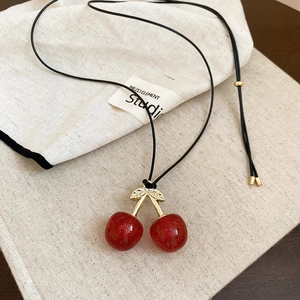 Close-up of red cherry pendant necklace with golden leaves on beige linen bag
