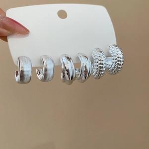 Macro detail of three pairs of silver-plated C-shaped earrings with unique textures