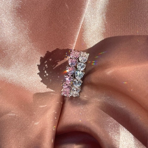 Macro shot of silver eternity rings with heart-cut pink and white stones on pink silk