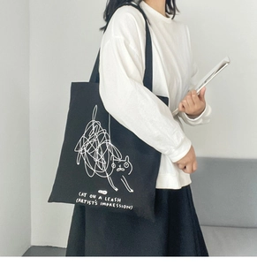 Detailed view of black canvas tote bag featuring white cat line art and artistic text
