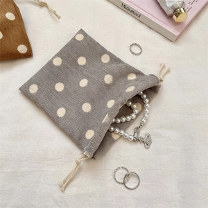 Close-up of grey polka dot corduroy drawstring pouch with pearl jewelry and soft lighting