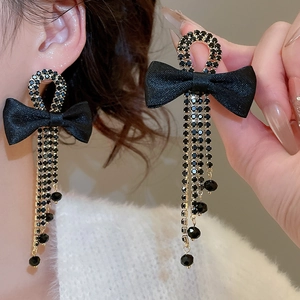 Detail of long black fabric bow earrings with sparkling rhinestone fringe on model