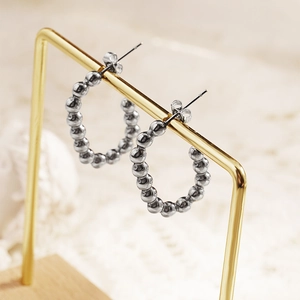 Chic silver beaded C-shaped hoop earrings on a metal display stand with textured background