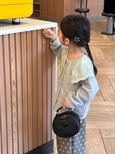 Detailed view of child wearing grey lace collar cardigan and black mini bow handbag