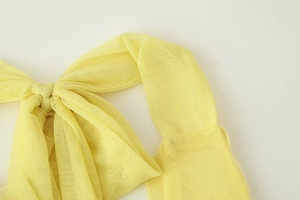 Close-up detail of a yellow mesh bow on a slim dress showing the fine fabric texture