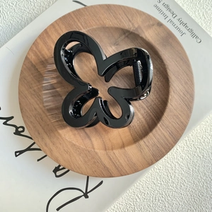 Detail of a sleek black butterfly hair claw clip resting on a rustic wooden display tray