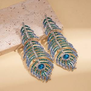 Détail des boucles d'oreilles plume de paon avec cristaux bleus sur support pierre