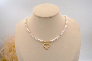 Close-up of a freshwater pearl necklace with a golden hollow heart pendant on a mannequin