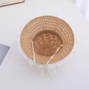 Detailed close-up of straw beach hat with white lace trim and adjustable chin strap