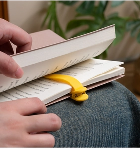 Action shot of the bright yellow silicone bookmark following the page on a pink book