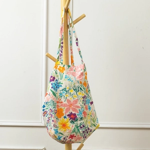 Detail of floral canvas tote bag with colorful rose patterns hanging on a wooden rack
