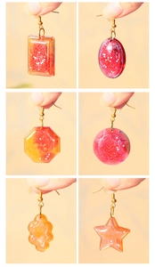 Detail view of handmade resin earrings with red-orange gradients and glitter in six shapes