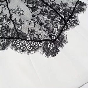 Macro view of black floral eyelash lace patchwork with small buttons on white fabric