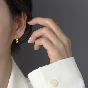 Close-up of golden twisted C-shaped earrings worn by a model in a minimalist style