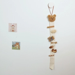 Detail of wall-mounted beige fabric hair accessory organizer with a brown plush bear