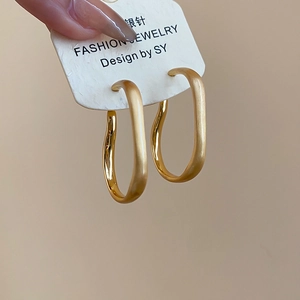 Detail of gold twisted oval hoop earrings with silver pins and matte metallic finish
