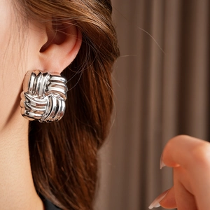 Detail view of a silver knotted textured earring worn on the ear showing metallic luster