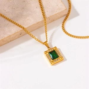 Detailed close-up of gold plated square green crystal pendant necklace on beige stone