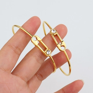 Polished gold safety pin bracelet with crystal zircon worn by a hand on white background