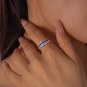 Detail of rose gold open ring featuring square blue sapphire and zircon on model finger