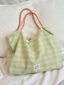Plaid canvas tote bag with orange rope handles on soft white bedding background