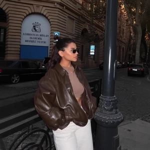 Outdoor night shot of a brown oversized faux leather bomber jacket with a zipper closure