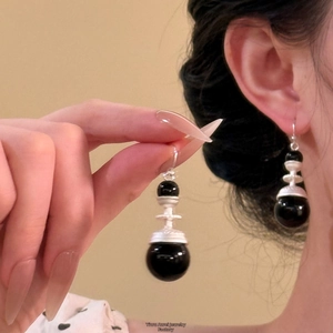 Dettaglio di orecchini a sospensione in pelle con metallo argento e perline nere lucide