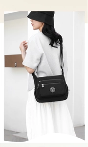 Side view of black nylon crossbody bag with multiple pockets worn by a female model outdoors
