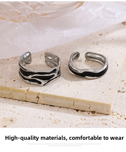Detail of two adjustable stainless steel rings with black enamel texture on beige stone