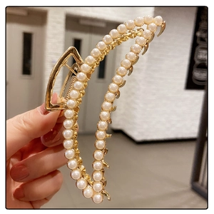 Macro view of a large gold metal shark clip featuring elegant white pearl embellishments