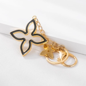 Golden clover car keychain with black enamel flower pendant on white geometric background
