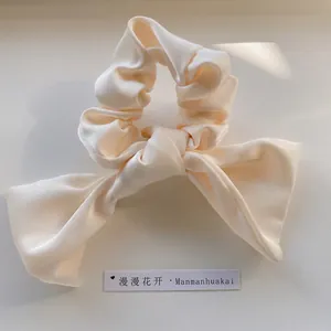 Detail of a creamy beige satin scrunchie with a large elegant bow and soft texture