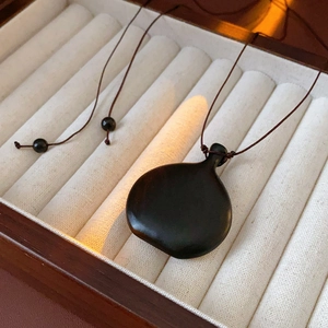 Detail of a dark wood gourd pendant necklace on a premium velvet jewelry box liner