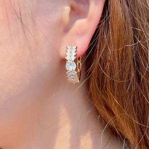 Détail des boucles d'oreilles créoles à double rangée de zircons dorés sur l'oreille