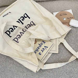 Detail of beloved embroidery on cream canvas tote bag with books and lifestyle items