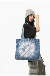 Detail of a large denim tote bag featuring cross-stitch patterns and raw frayed edges