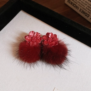 Macro view of red resin flower and fluffy pom pom earrings on a soft velvet tray
