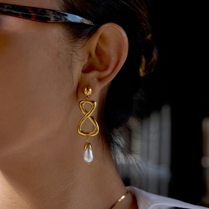 Boucles d'oreilles infini dorées avec perle pendante portées par un mannequin