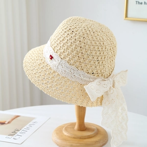 Beige woven straw sun hat with white lace ribbon bow and small flower on wooden stand